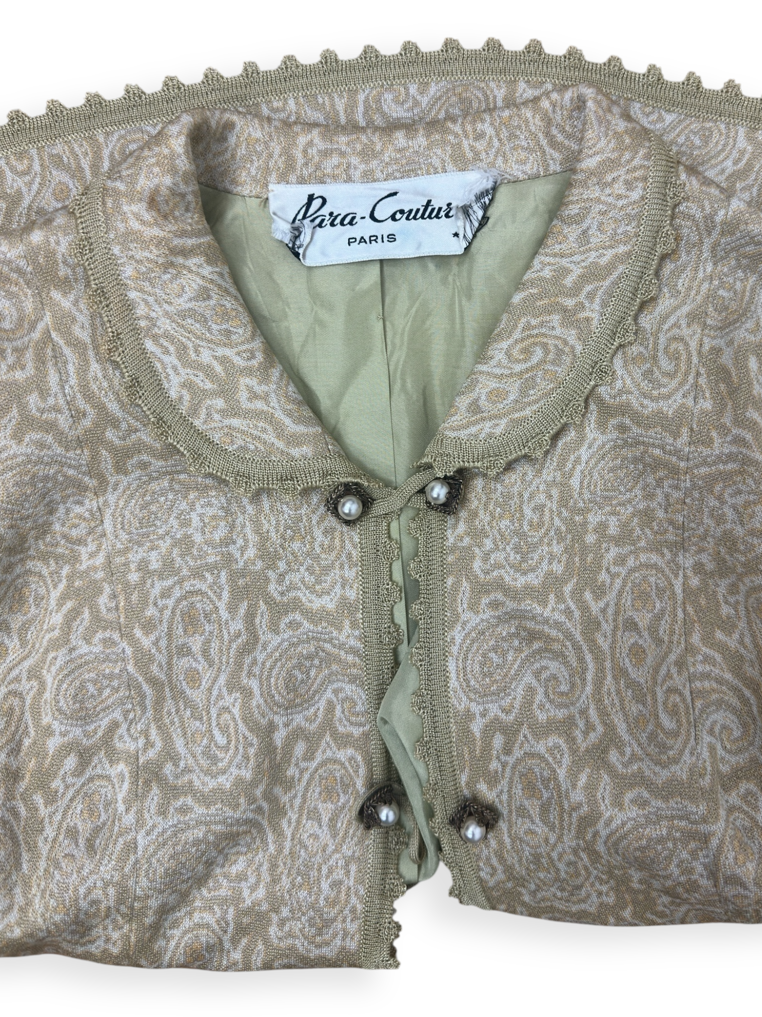 Veste boho vintage Para-Couture Paris, confectionnée en France dans un jacquard paisley beige et ivoire rehaussé d’un fil doré. Boutons perles sertis, finitions crochetées et bordure festonnée. Une pièce féminine et délicate, typique des créations parisiennes des années 60. État excellent. Parfaite sur une robe fluide ou un jean taille haute. | Paris Bonheur